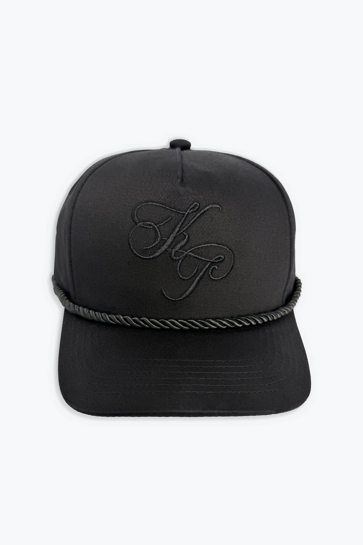 A black baseball cap featuring a black rope detail wrapped around the base of the crown and a tonal embroidered monogram logo on the front, set against a plain white background.