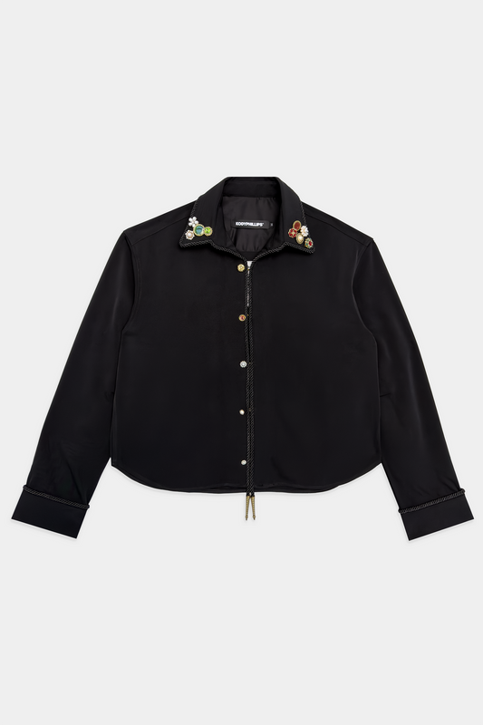 A black slightly cropped button-up shirt jacket with decorative colorful buttons and embellishments on the collar, displayed flat against a light gray background.