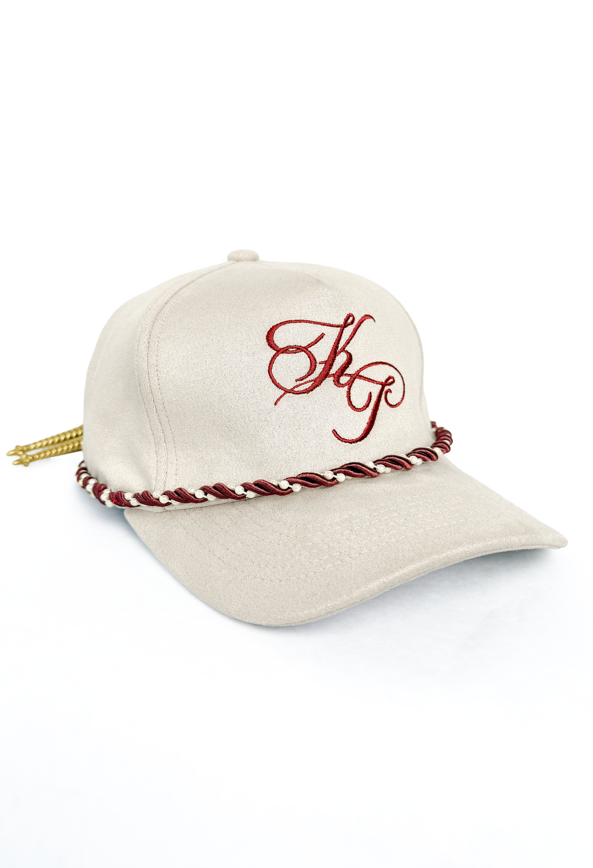 An ivory baseball cap featuring a red embroidered monogram on the front, a red and white braided rope detail around the base of the crown, and a gold tassel hanging from the side, set against a plain white background.